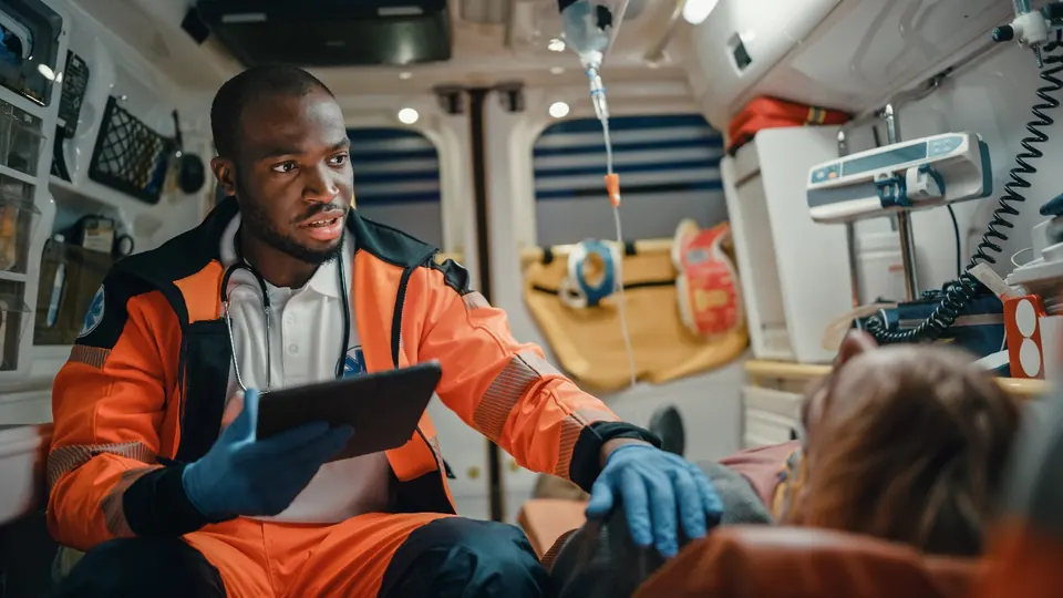 A paramedic with a tablet reassuring a patient in the back of an ambulance