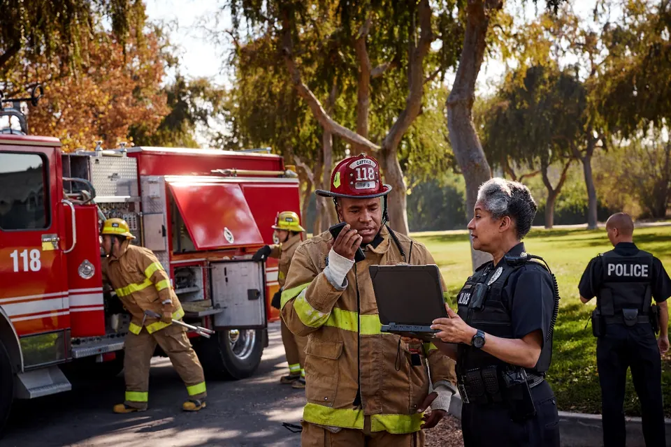 A fire captain with a radio and a laptop conferring with a police officer at an incident scene